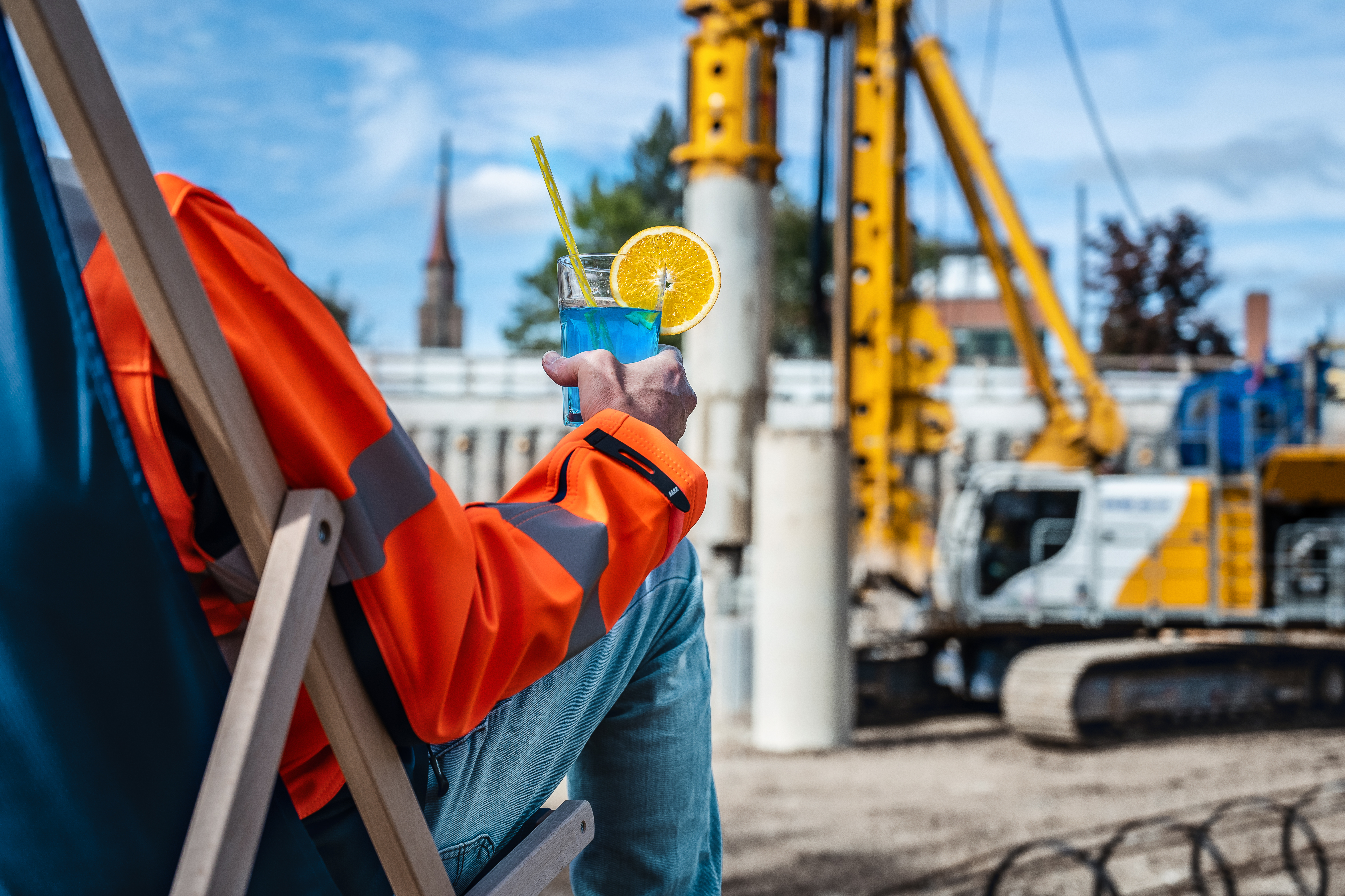 Blauer Cocktail in der Hand, Baustelle im Hintergrund. Beitragsbild zur IFAT 2026 mit Kundenevent von Bauer Resources.