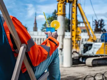 Blauer Cocktail in der Hand, Baustelle im Hintergrund. Beitragsbild zur IFAT 2026 mit Kundenevent von Bauer Resources.